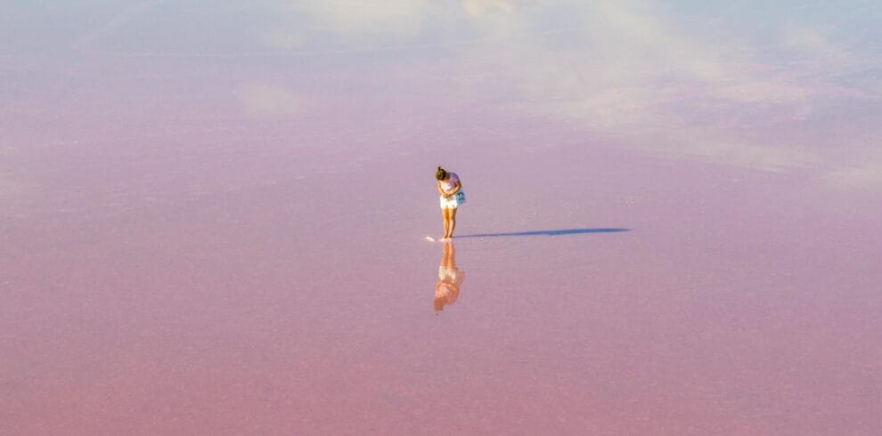 A woman stands on a vast pink salt lake, reflecting clouds in Dimboola, Australia.