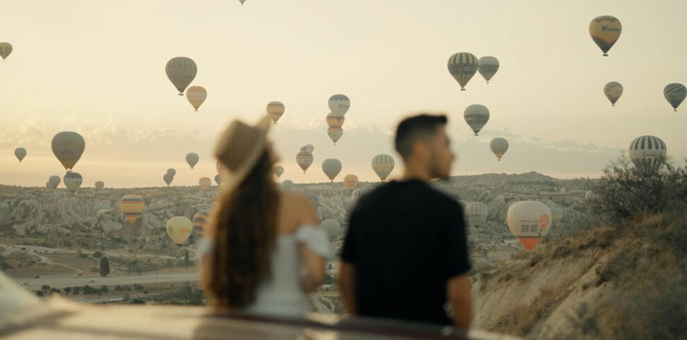 Couple watching hot air balloons at sunrise in Cappadocia, Türkiye, a popular travel destination.