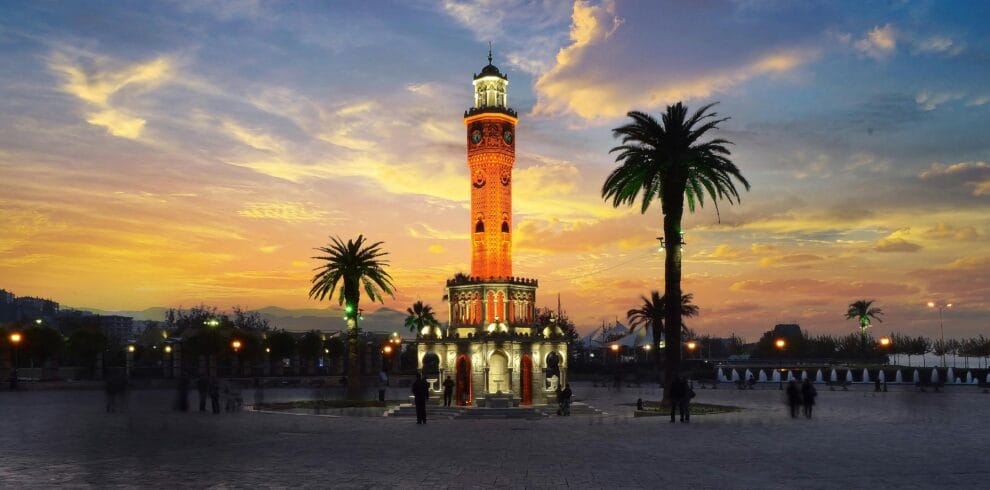 Stunning view of Izmir's iconic clock tower glowing at sunset, surrounded by palm trees.